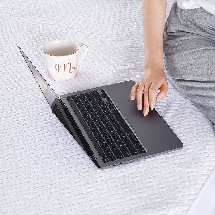 A woman sits on a bed with IHanherry waterproof mattress protector and uses a computer